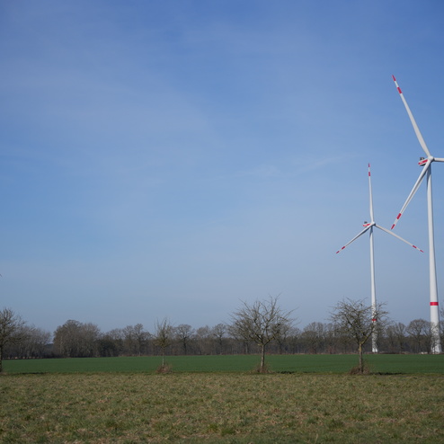 Drei Windkraftanlagen stehen in einem gr&uuml;nen Feld unter blauem Himmel mit wenigen Wolken.