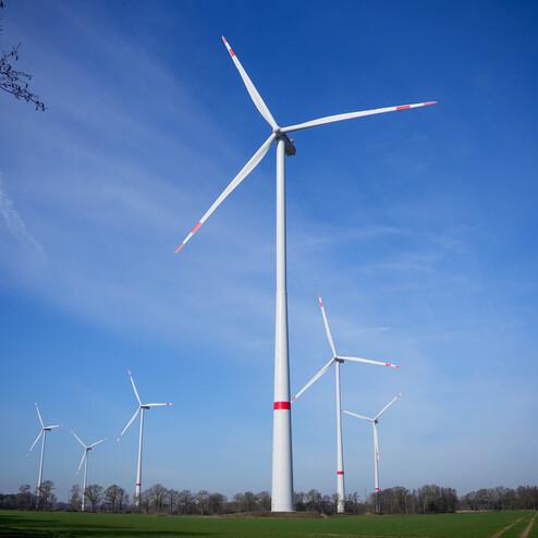 F&uuml;nf Windkraftanlagen stehen auf einem Feld vor einem blauen Himmel mit einzelnen Wolken.