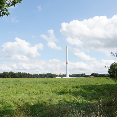 Zwei Windkraftanlagen stehen auf einer Wiese unter einem wolkigen Himmel. Gr&uuml;ne Landschaft im Hintergrund.
