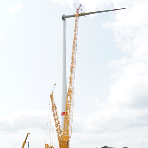 Kran montiert eine Windturbine auf einem Feld, blauer Himmel mit Wolken im Hintergrund.