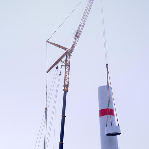 Kran hebt einen zylindrischen Schornstein mit rotem Streifen &uuml;ber einer nebligen Landschaft.