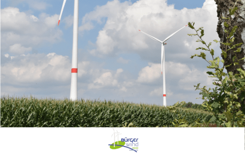 Zwei Windkraftanlagen hinter einer Maisfeldkante unter einem bew&ouml;lkten Himmel. Logo von B&uuml;rgeer Wind unten.