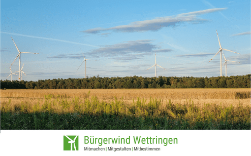 Windr&auml;der stehen neben einem Feld mit goldgelbem Getreide, umgeben von B&auml;umen und blauem Himmel.