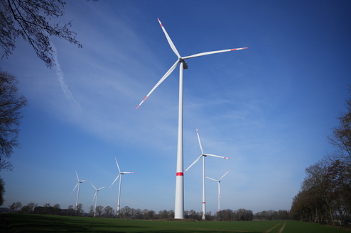 F&uuml;nf Windkraftanlagen stehen auf einem Feld unter blauem Himmel mit wenigen Wolken.
