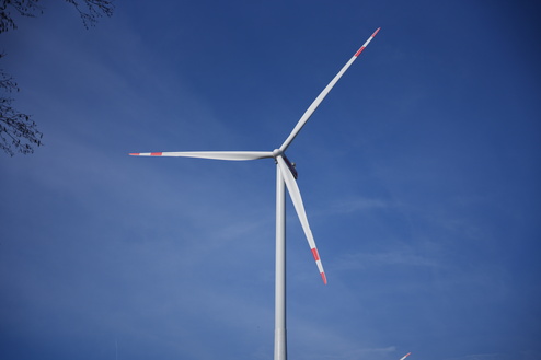 Nahaufnahme eines Windrads mit rot-wei&szlig;en Bl&auml;ttern vor einem blauen Himmel.