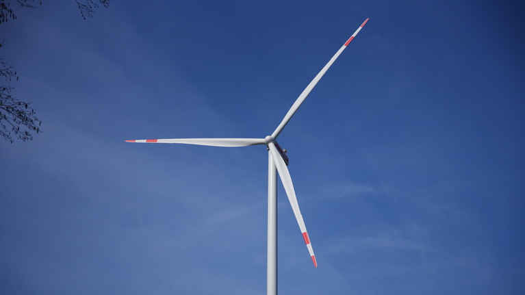 Nahaufnahme eines Windrads mit rot-wei&szlig;en Bl&auml;ttern vor einem blauen Himmel.