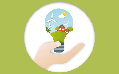 Hand h&auml;lt eine Gl&uuml;hbirne mit einer Landschaft, Windkraftanlagen und H&auml;usern in einem gr&uuml;nen Umfeld.